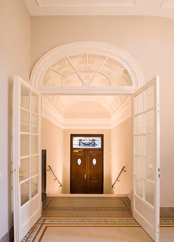 Open double glass doors leading to stairs descending to a wooden door with stained glass window.
