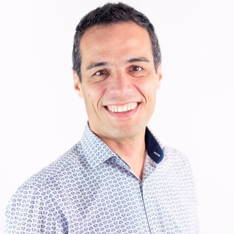 Homme souriant portant une chemise blanche à motifs bleus sur fond blanc.