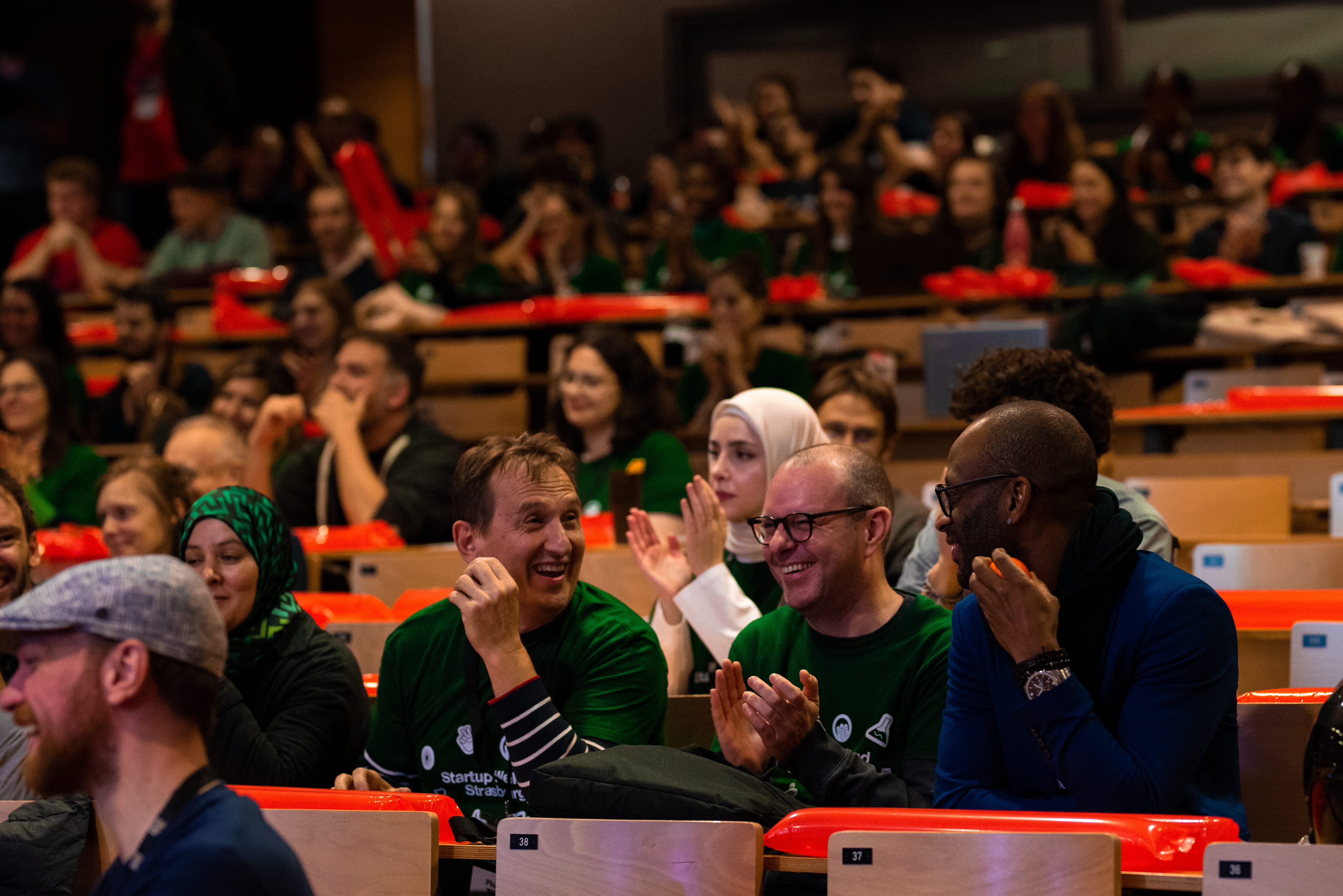 Des personnes assises souriantes et applaudissant lors d'un événement dans une salle de conférence.
