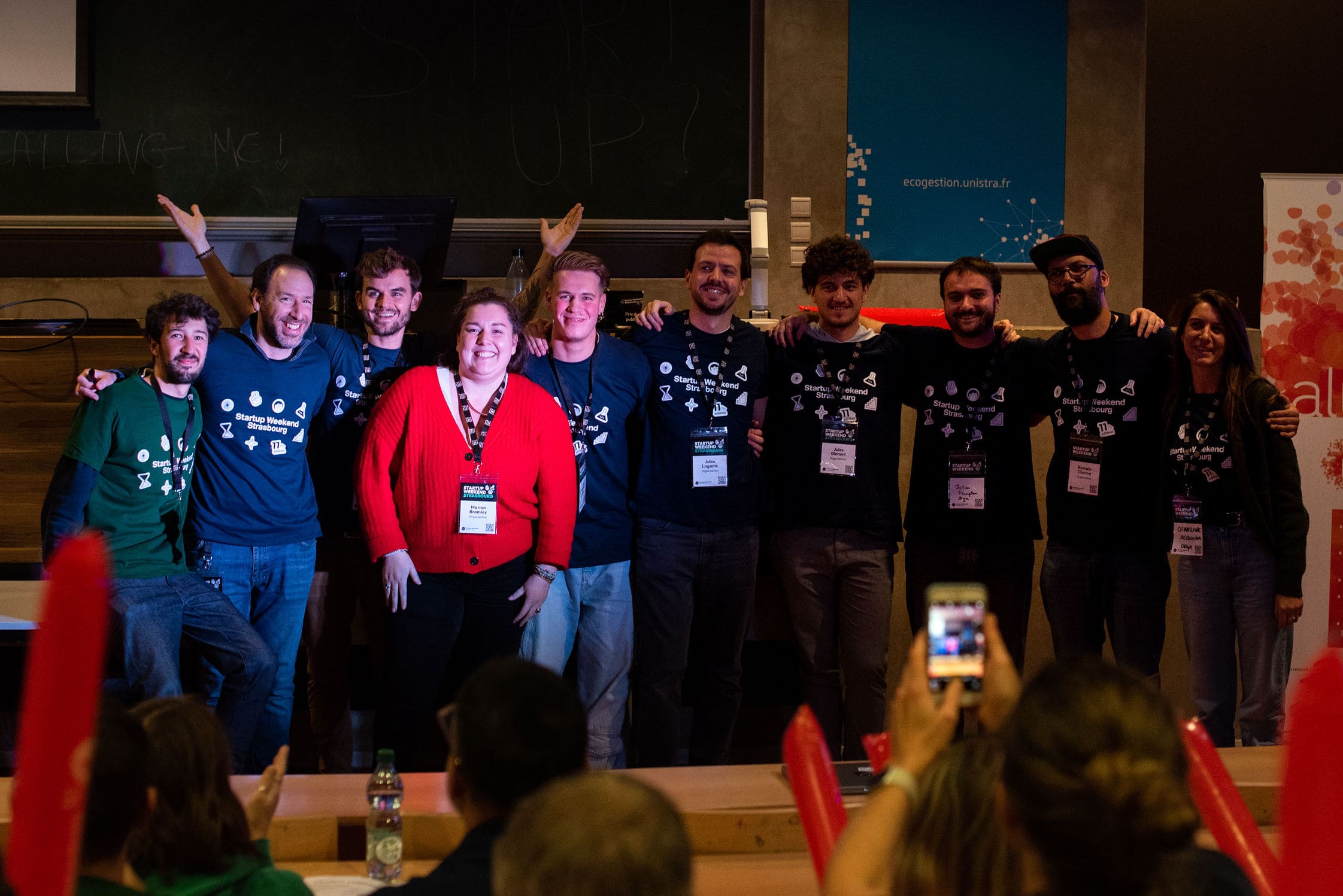 Groupe de dix personnes souriantes posant sur une scène lors d'un événement Startup Weekend Strasbourg.