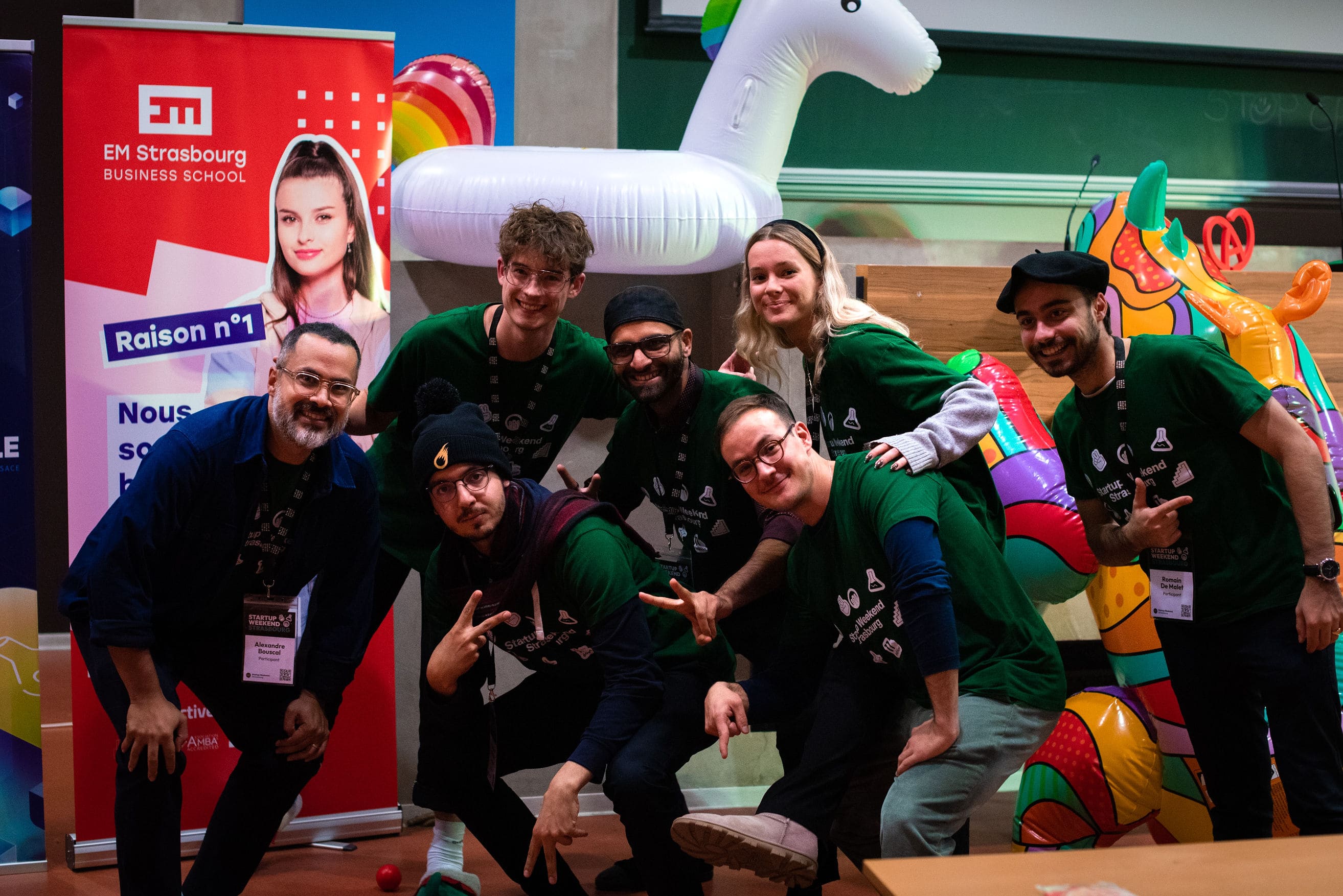 Groupe de sept personnes souriantes en t-shirts verts posant devant un ballon licorne gonflable coloré.