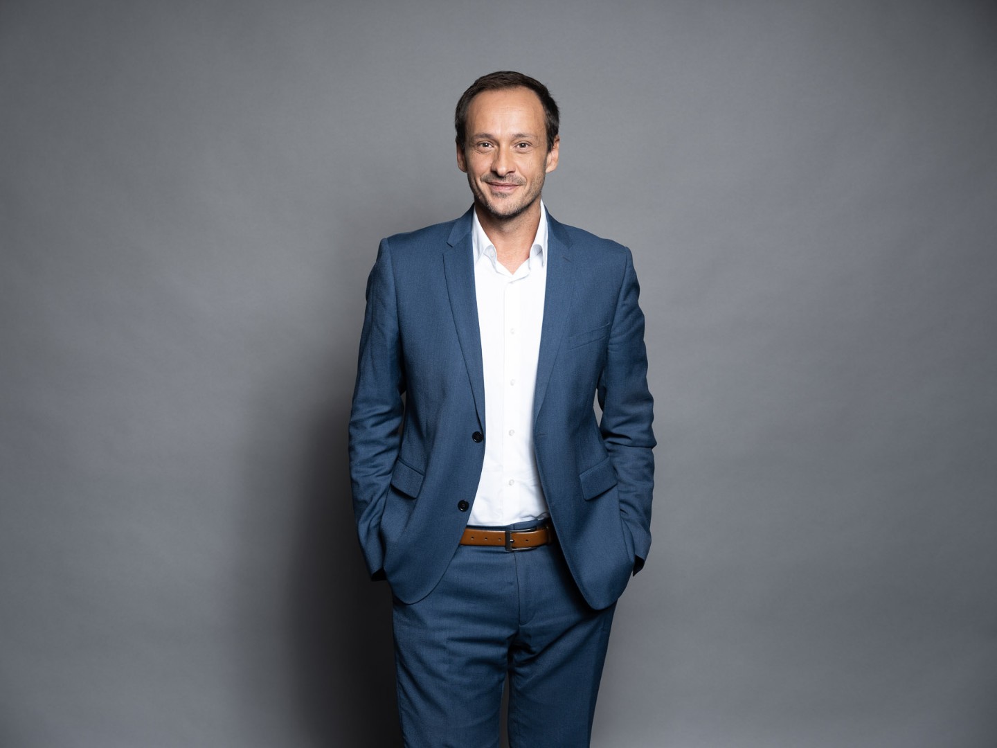 Homme souriant portant un t-shirt noir devant un fond gris uni.