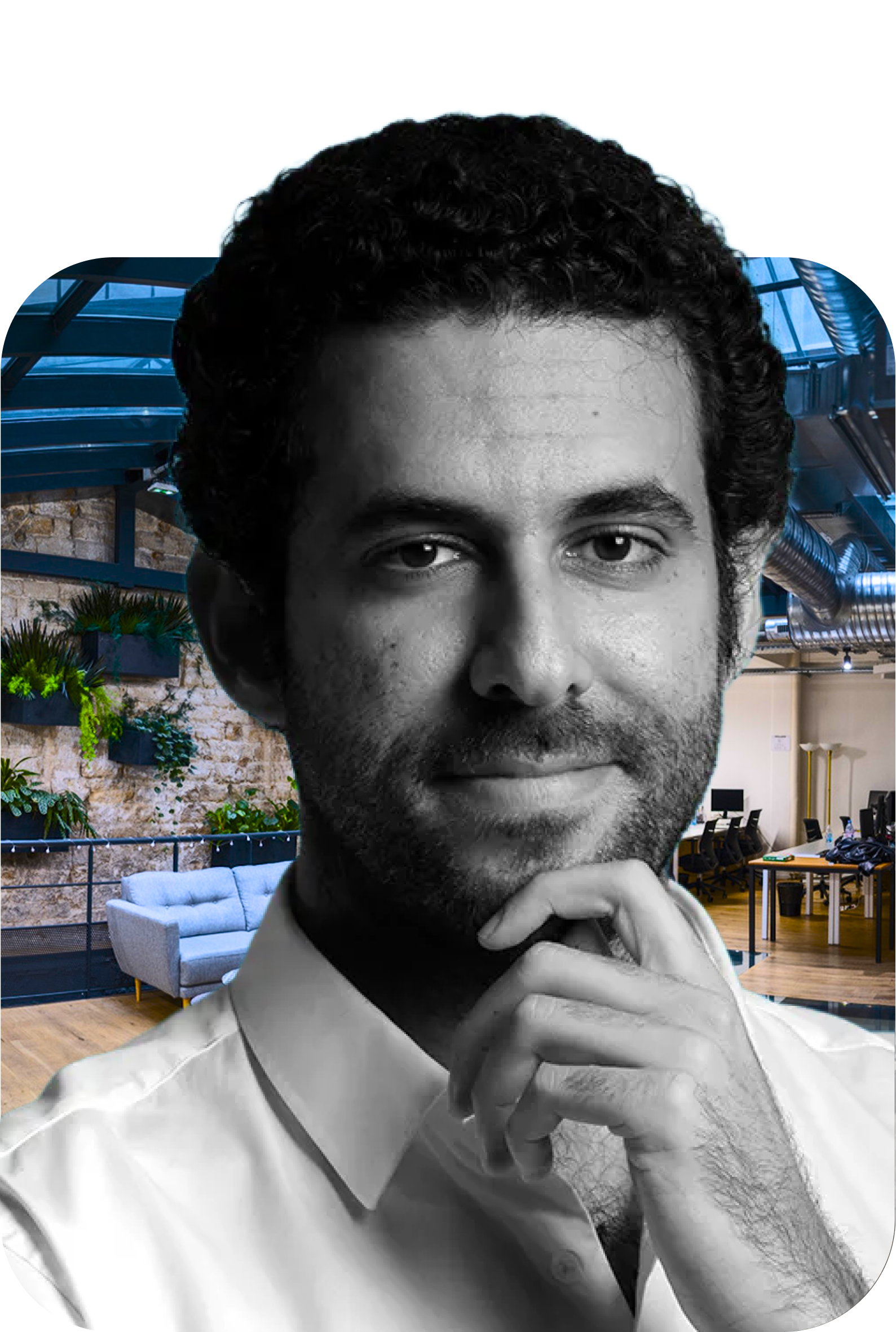 Homme pensif avec barbe et chemise blanche devant un bureau moderne avec plantes et canapé.