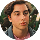 Jeune homme aux cheveux bruns, regardant à gauche avec un fond flou de feuillage vert.