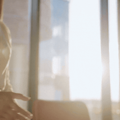 Person extending hand indoors with bright sunlight streaming through large windows in the background.