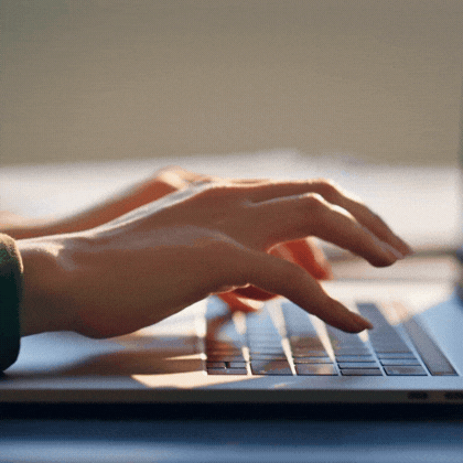 Hands typing on a laptop keyboard with soft natural light falling on them.