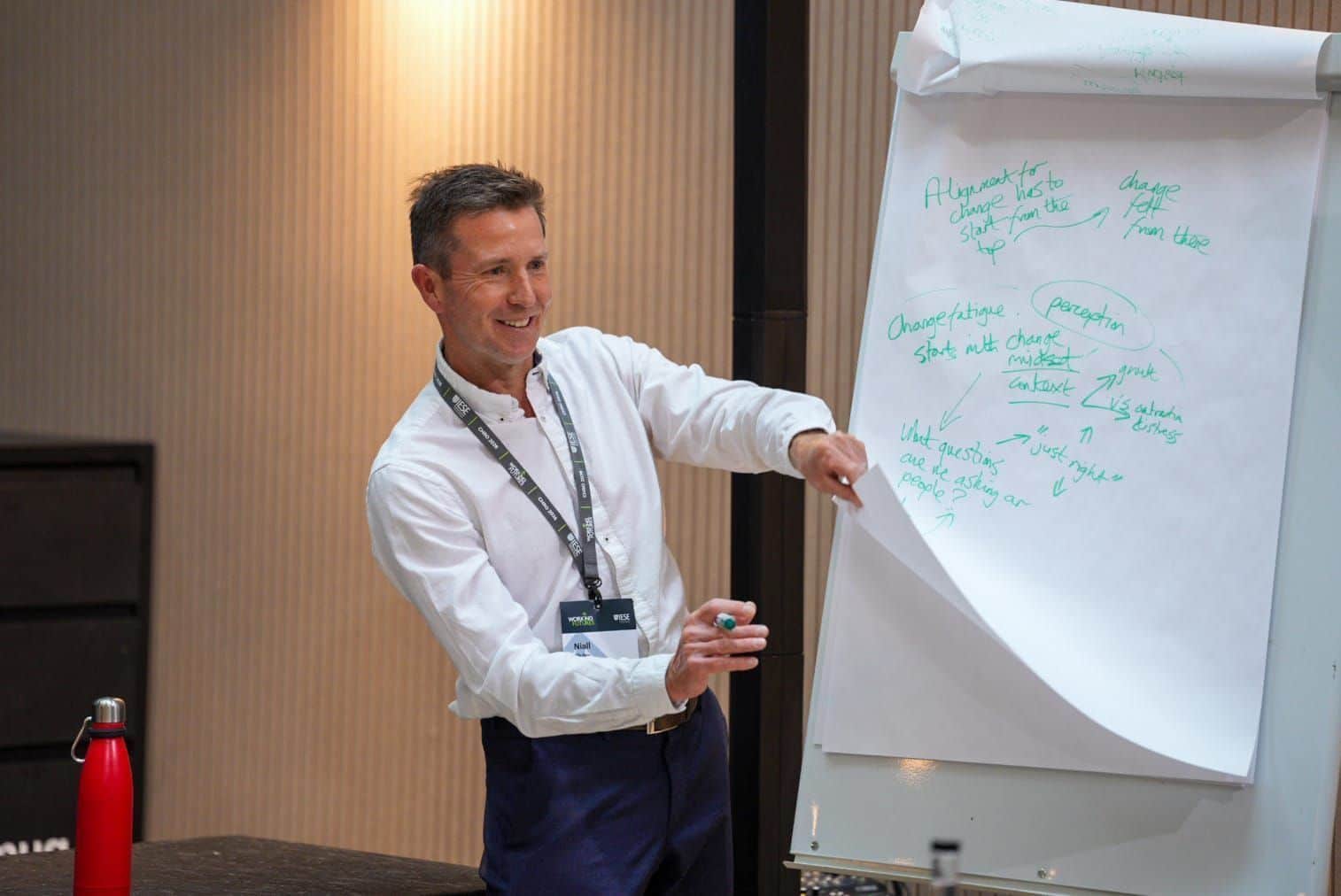 Man in white shirt presenting handwritten notes on a flip chart in a conference room.