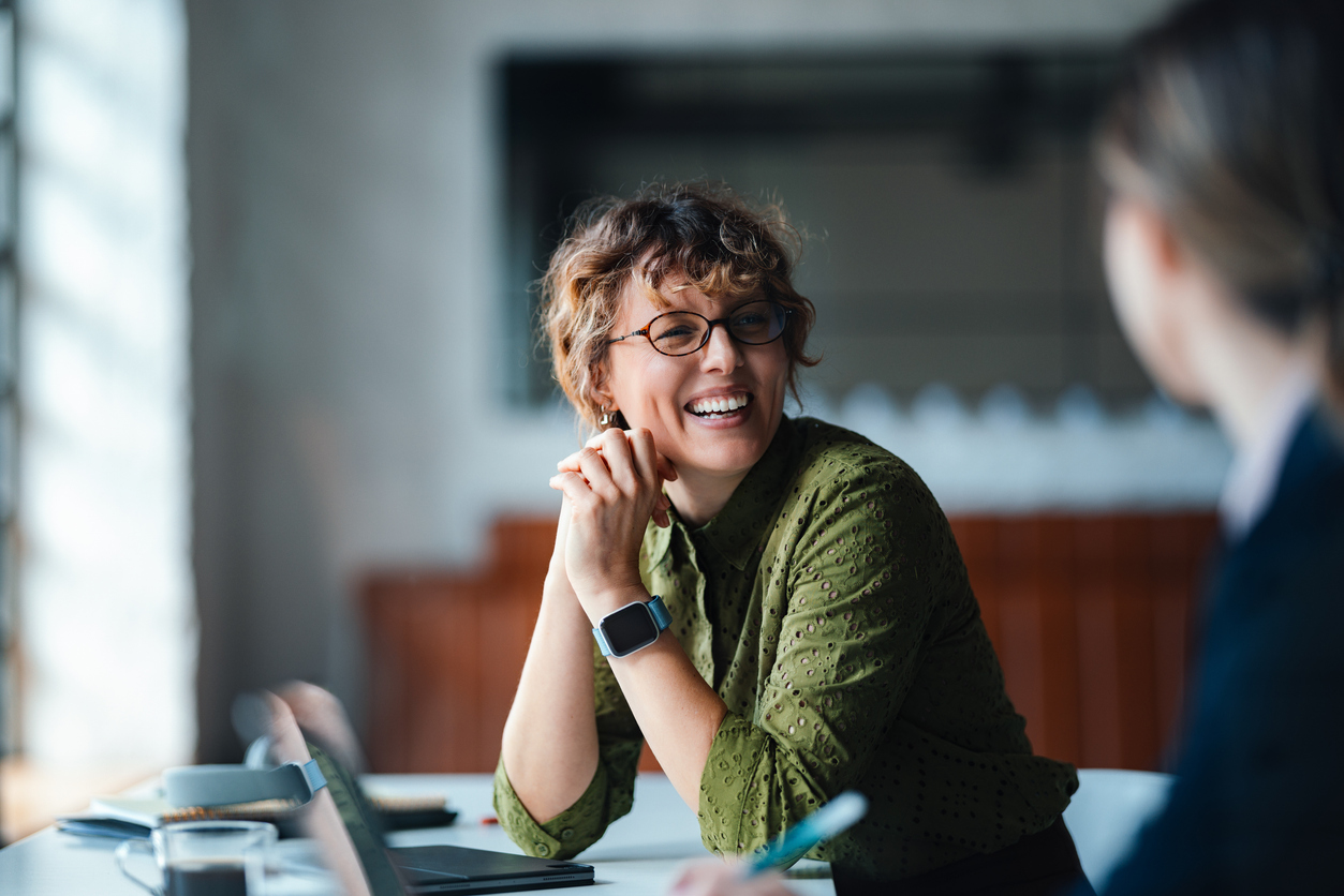 Woman with glasses and curly hair closely examining a green circuit board.