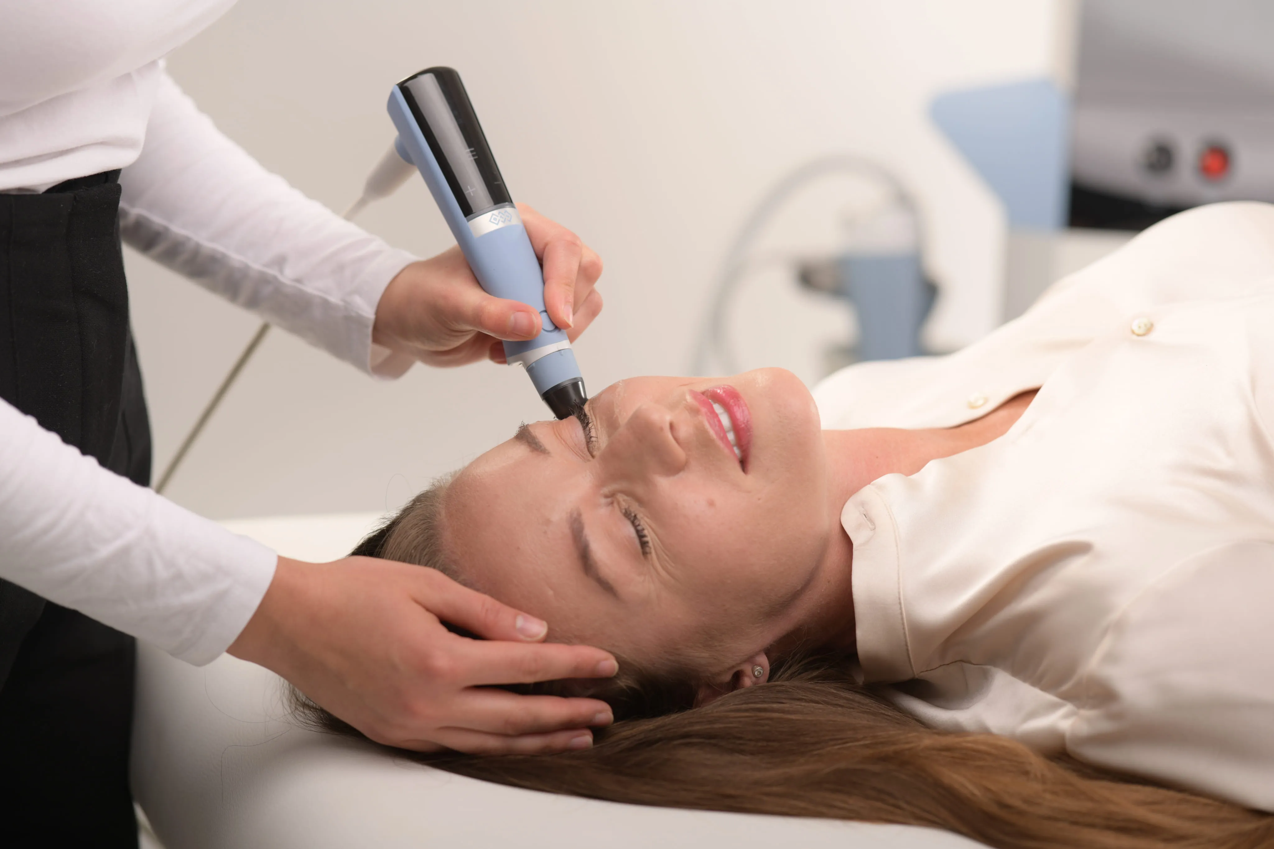 Woman lying down receiving a facial treatment near the eye with a handheld device.