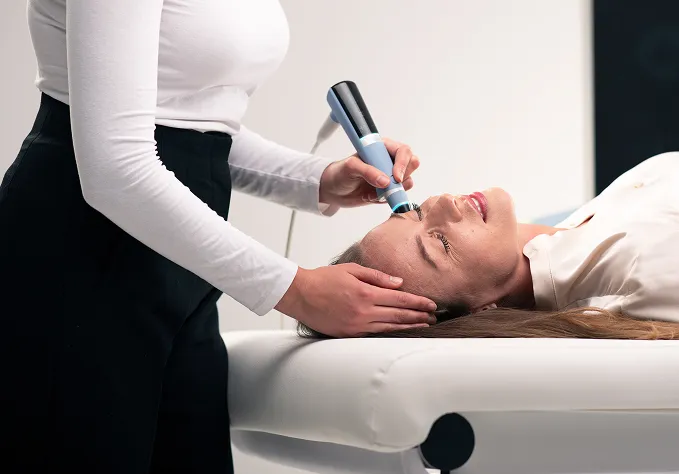 Woman receiving a facial treatment with a handheld device from a specialist in a clinic.