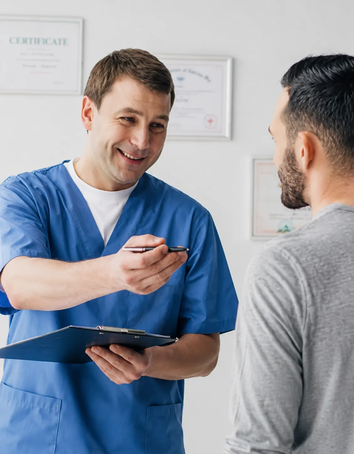 Klinikpersonal i blå arbetsuniform diskuterar behandlingsprotokoll med patient under (BTL, rehabilitering).