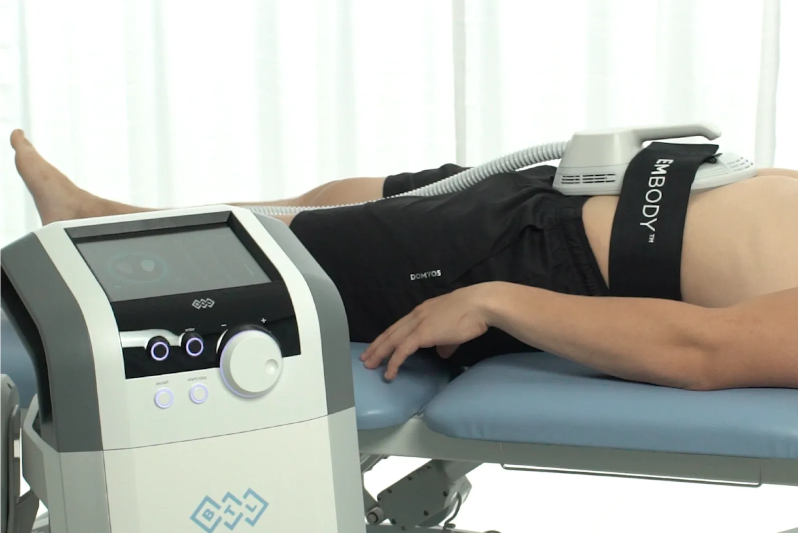 Patient genomgår HIFEM-muskelstimuleringbehandling med BTL EMBODY-applikator på armen medan behandlingsenhetens displaypanel