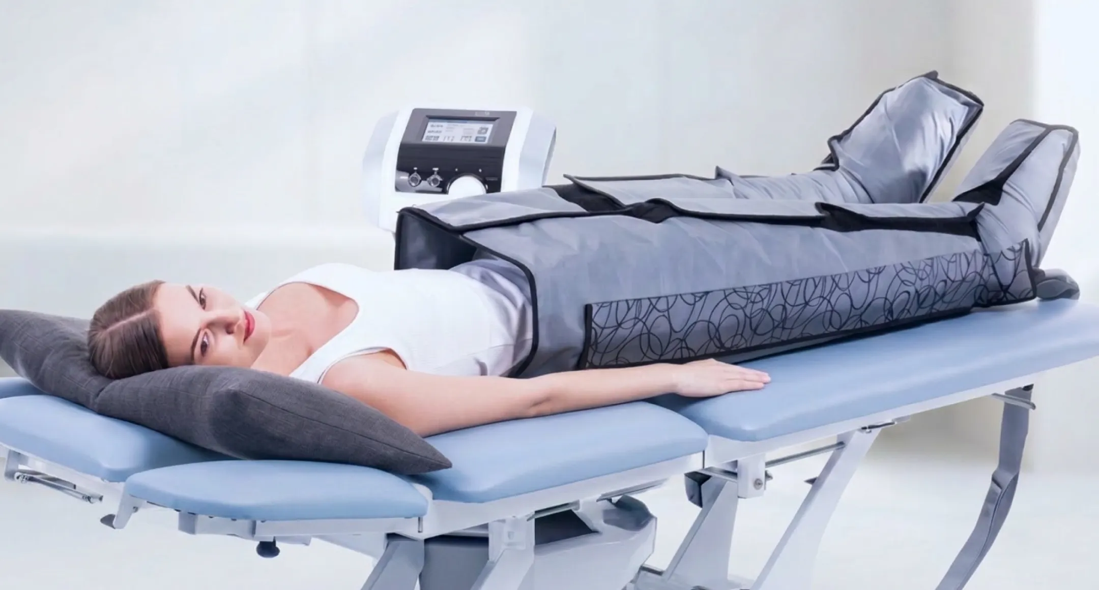 Patient ligger på behandlingsbrank med BTL Lymphastim pressoterapi-manschettar på ben och höft, pneumatisk kompressionsenhet