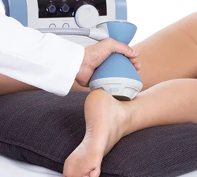 Therapist using blue shockwave therapy device on a patient's Achilles tendon area.