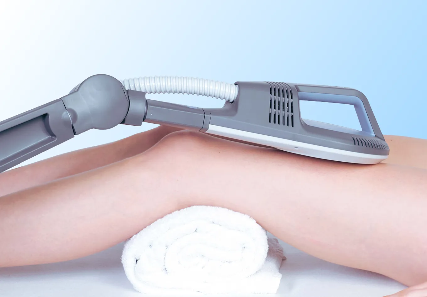 Device applying therapy on a bent knee resting on a rolled white towel against a blue background.