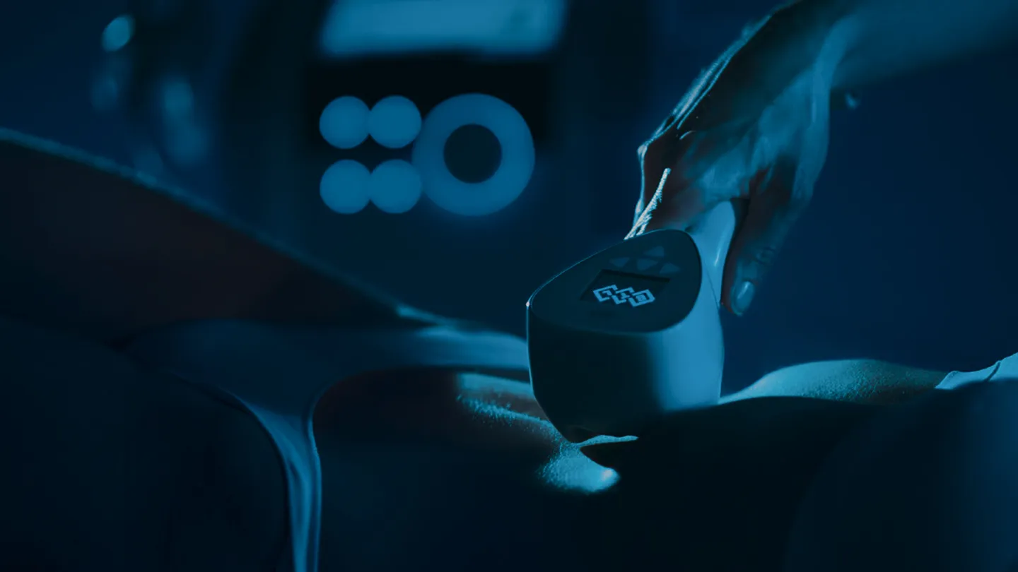 Close-up of hand holding a device on a person's upper back in a dark blue light setting.