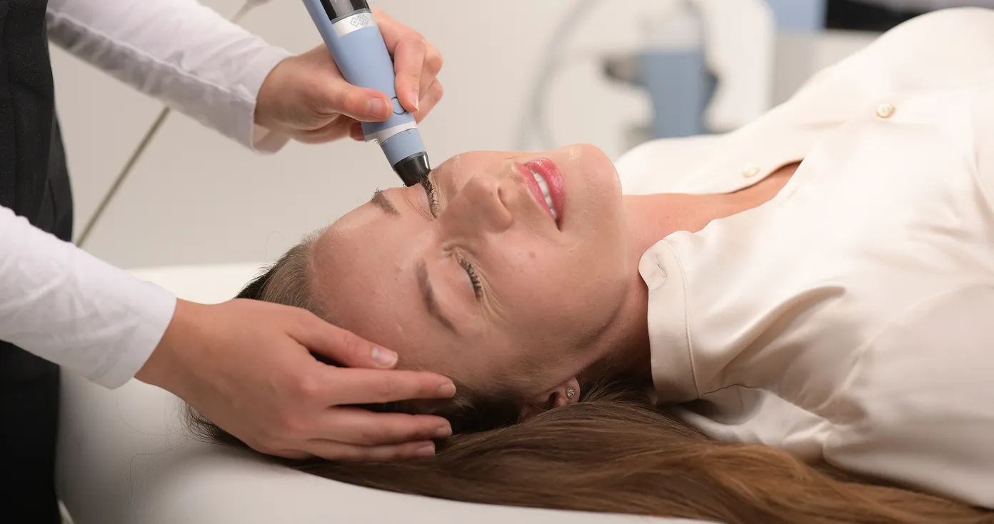 Woman receiving a gentle cosmetic treatment on her forehead using a handheld device.