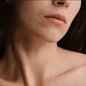 Close-up of a woman's neck and collarbone with smooth skin and dark hair.
