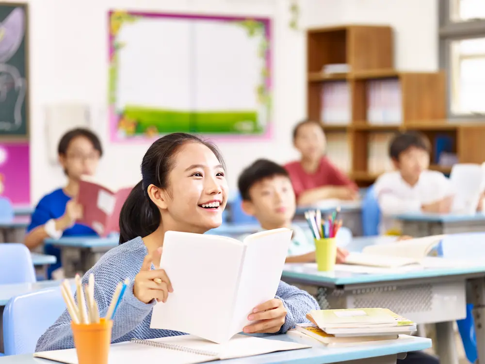 Children engaged in a group activity in a bright classroom with a teacher observing and smiling.