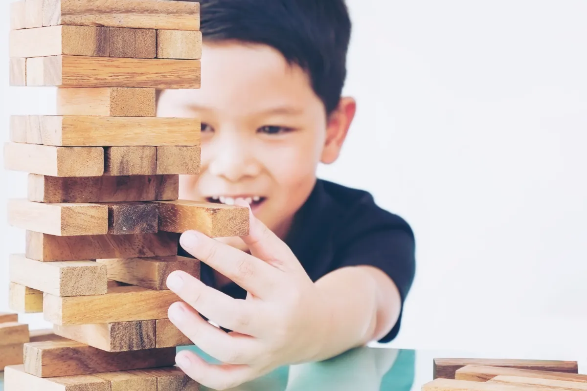 An Asian boy in Singapore carefully building a wooden block tower, practising problem-solving