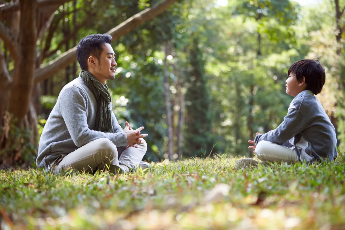An Asian father and child having a relaxed conversation outdoors, helping the child form and share an opinion