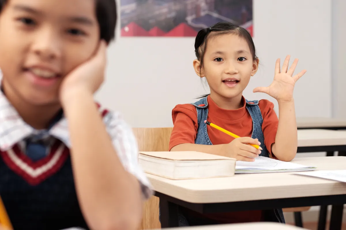 Asian primary school students in a classroom, pupils enthusiastically raising their hands to participate in discussion