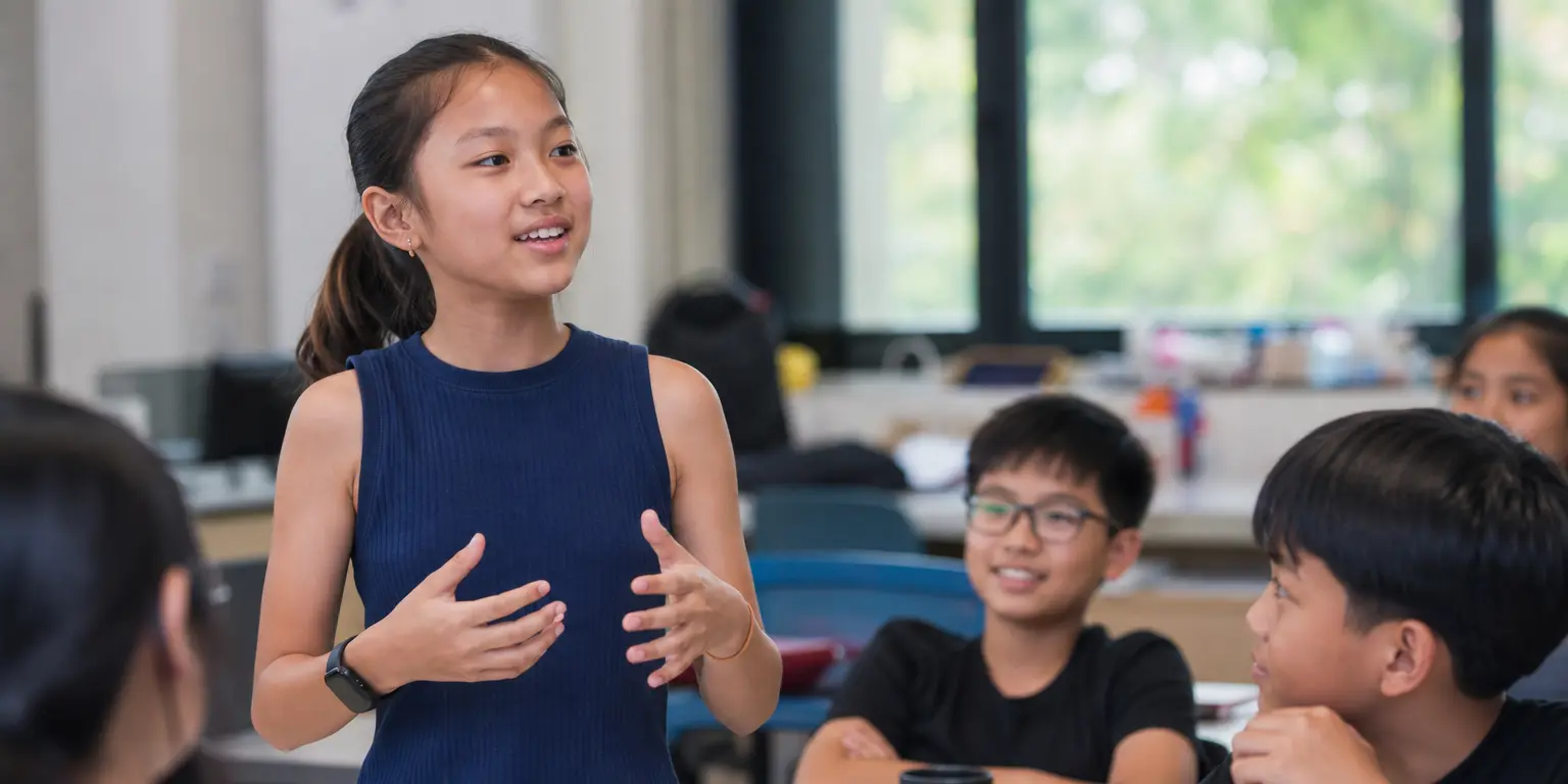 confident Singaporean Asian preteen, about 11 years old, standing and speaking naturally mid-presentation in a bright modern classroom