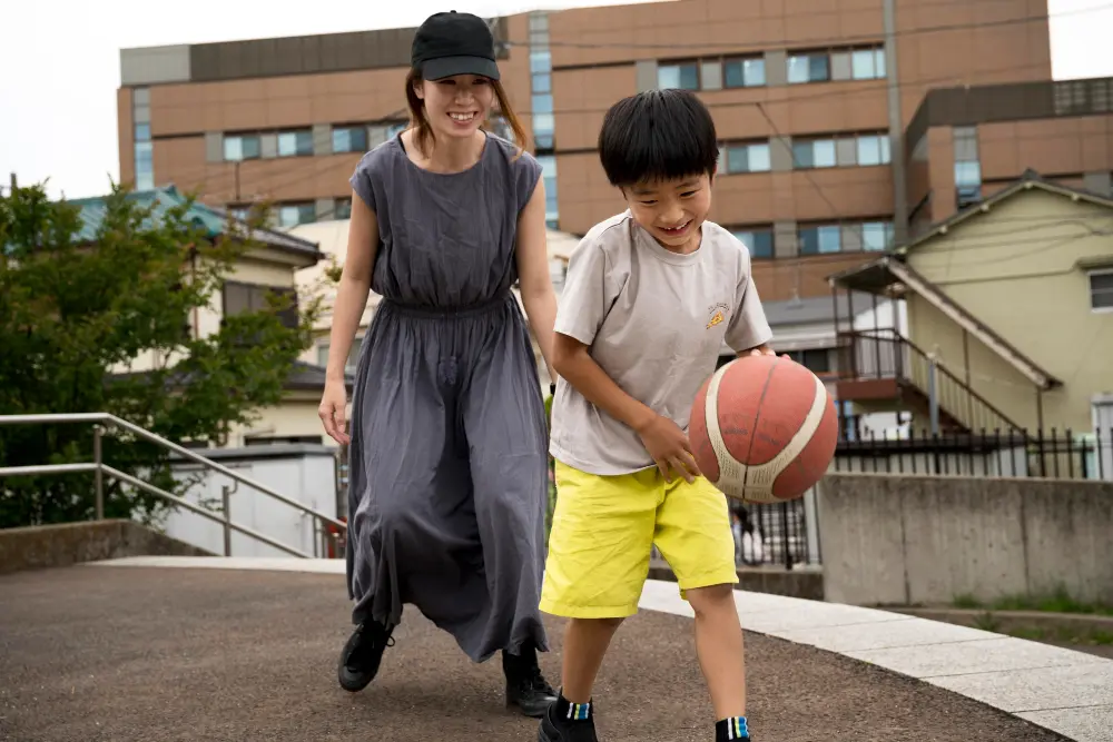 A mother and her young son smiling as they play basketball together outdoors