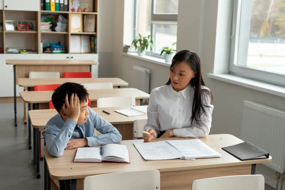 A teacher giving feedback to a primary school boy at his desk in a classroom