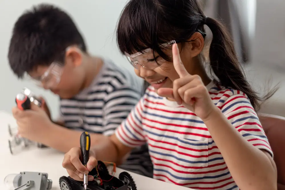 Children engaged in a group activity in a bright classroom with a teacher observing and smiling.