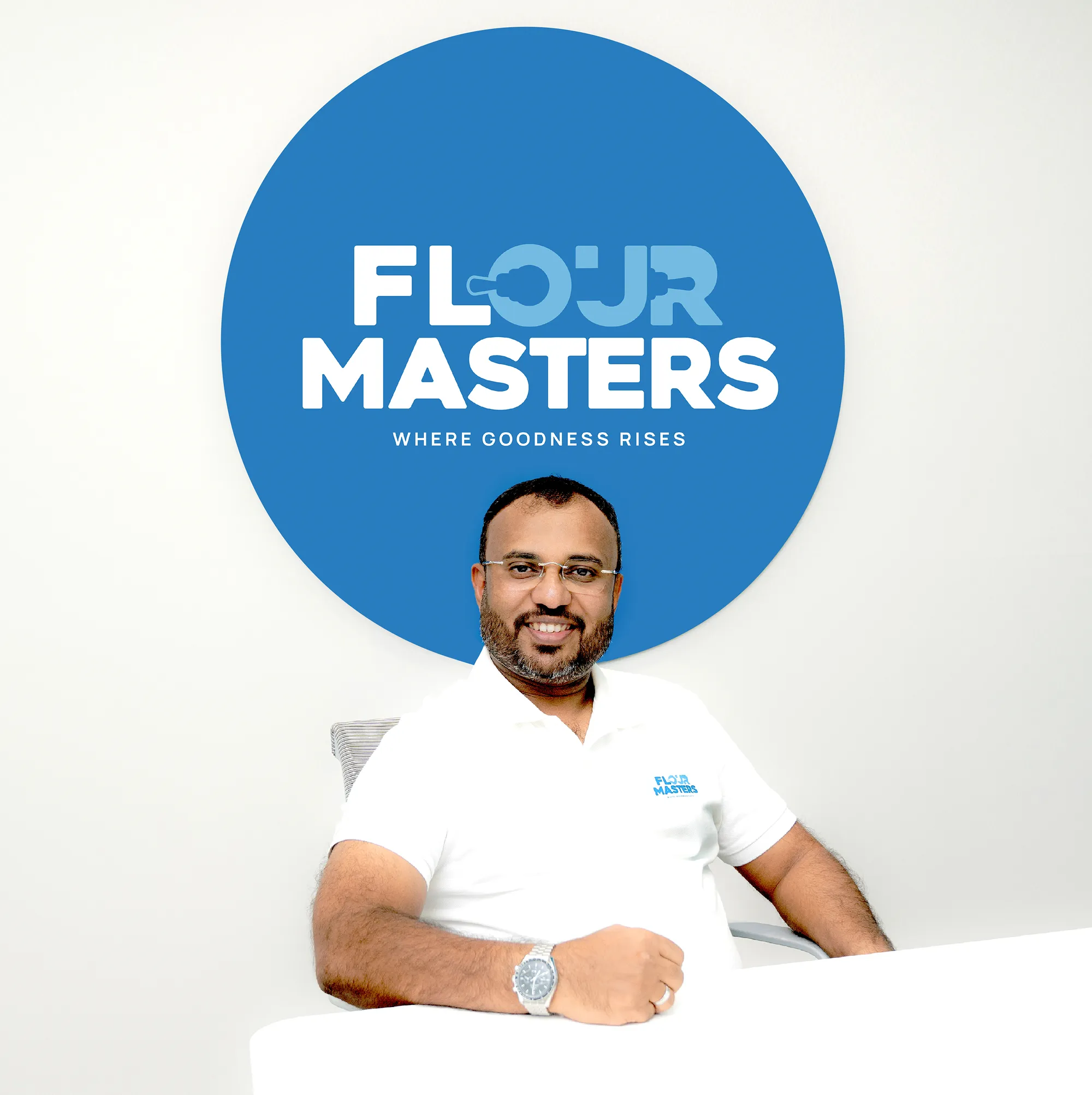 Man with glasses and beard seated smiling, wearing a white shirt with Flour Masters logo.