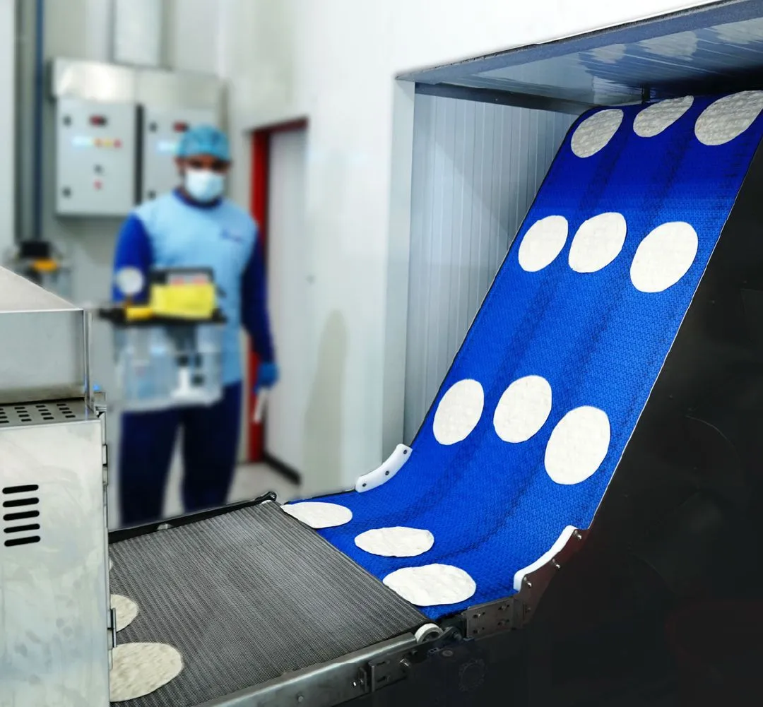 Industrial conveyor belt with round flatbread or tortillas being processed in a food factory.