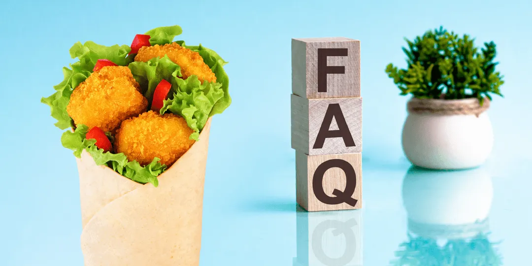 Wrap with fried chicken nuggets, lettuce, and red peppers with wooden blocks spelling FAQ and a small plant.