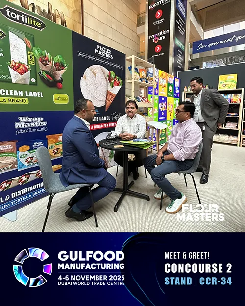 Four men in business attire sitting and standing around a table at a Flour Masters booth at Gulfood 2025.