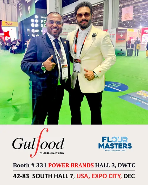 Two men in suits posing with thumbs up at Gulfood 2026 exhibition in a green-carpeted hall.