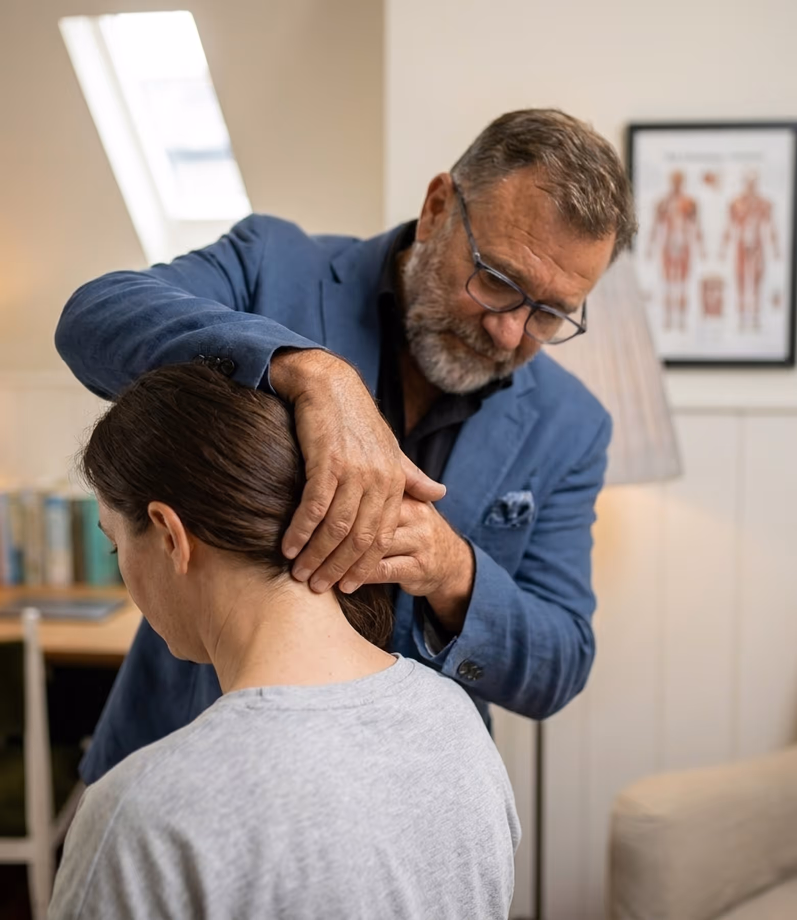 Man in glasses and blue jacket examining back of woman’s neck in a medical office.