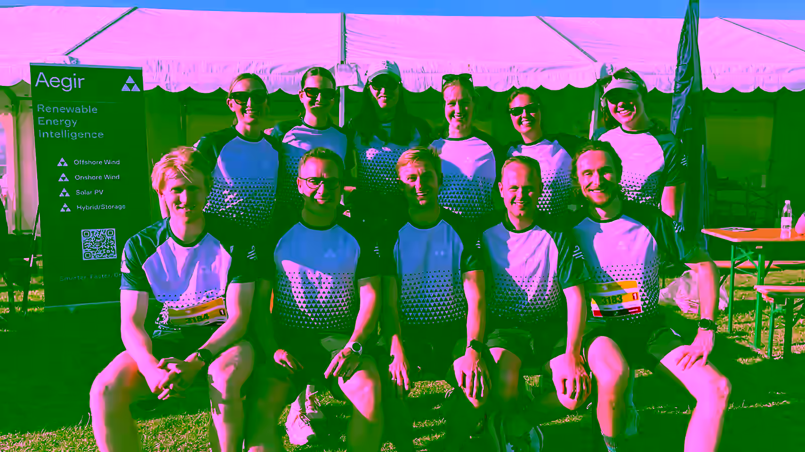 The Aegir Insights team of eleven in navy-and-lavender running shirts at the 2026 DHL relay run in Copenhagen, in front of the race tents next to the Aegir Renewable Energy Intelligence rollup banner.
