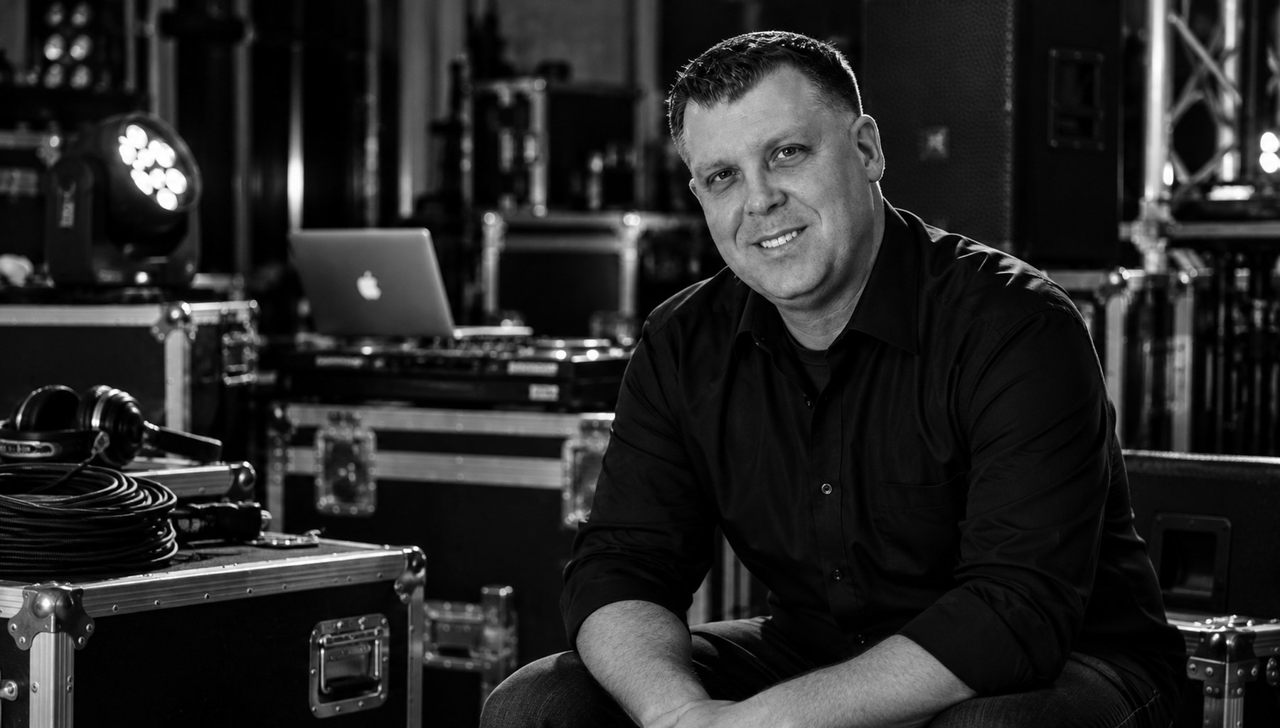 DJ Greg Williams seated among road cases, lighting and DJ gear