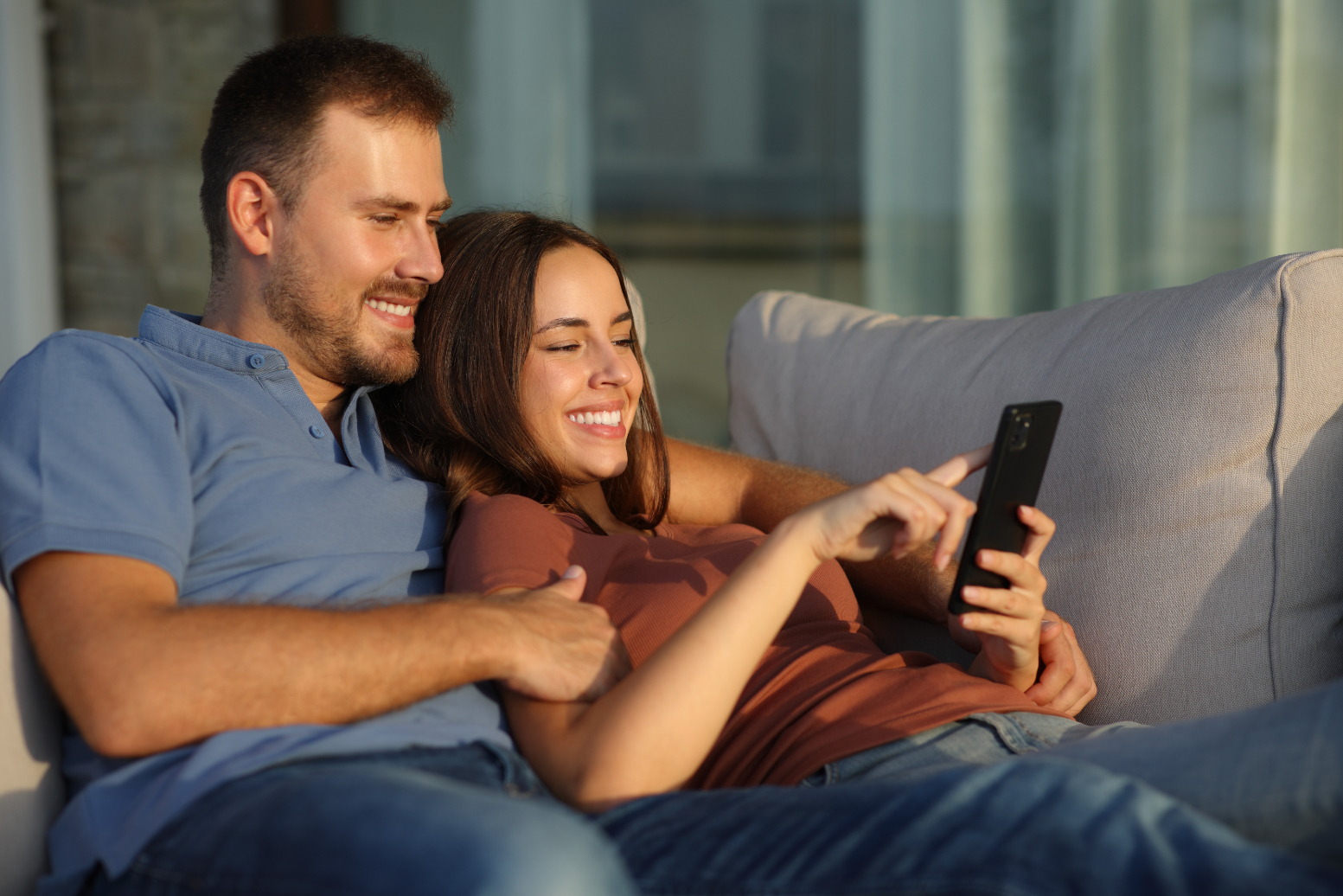 Couple sitting on sofa looking at phone stock image