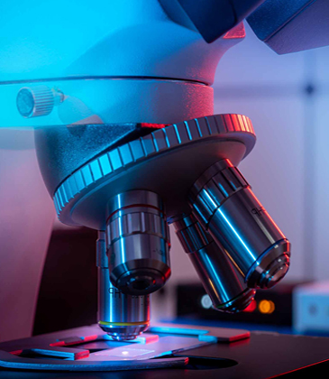 Close-up of a microscope lens with colorful blue and red lighting in a lab setting.