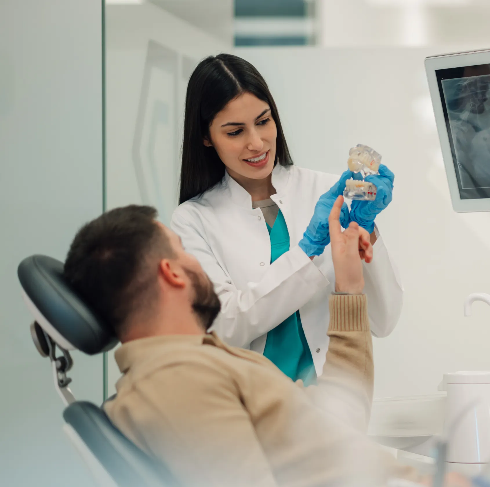 Female dentist showing dental model to seated male patient in dental office.