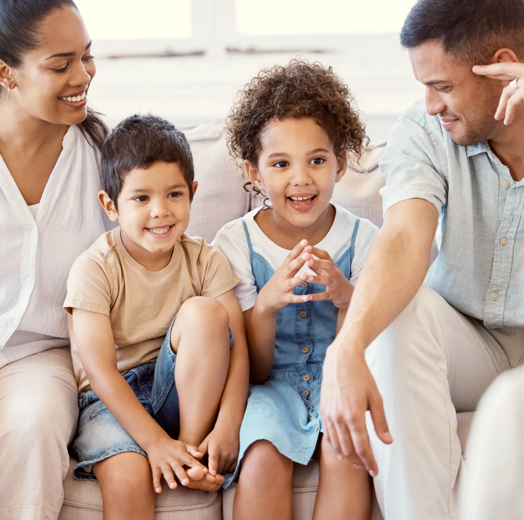Smiling family of four sitting closely together on a couch in a bright room.