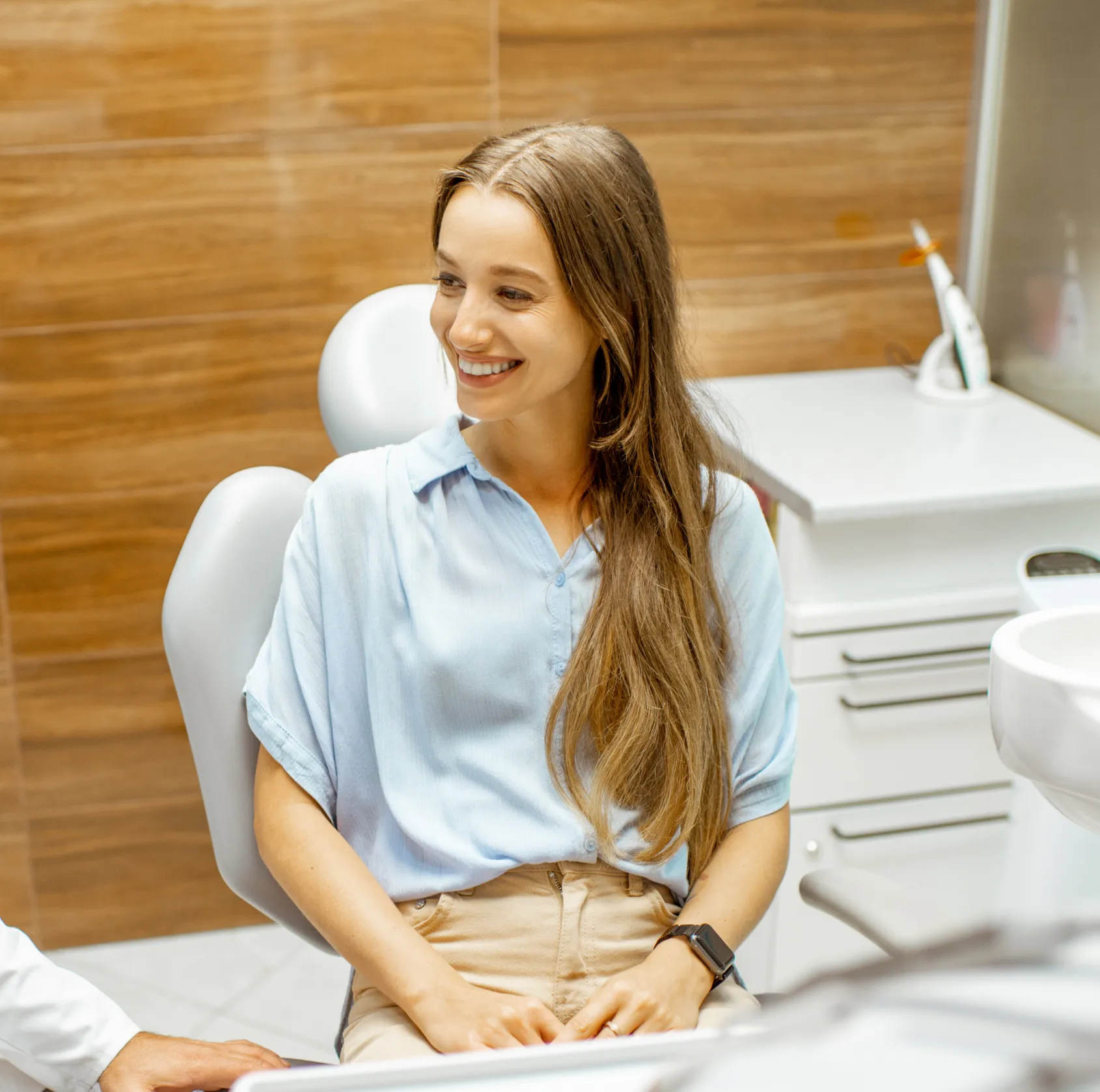 Smiling woman with long hair sitting in a dental chair in a dental office with wooden walls.