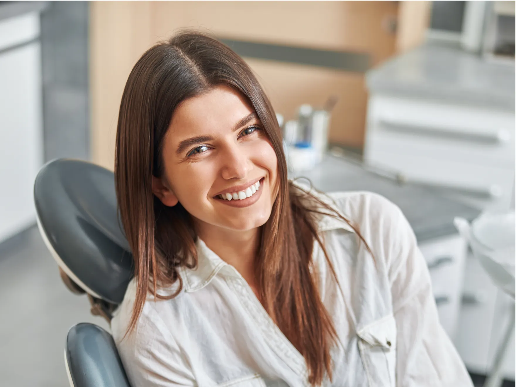 Smiling woman with straight brown hair sitting in a dental chair in a clinic.