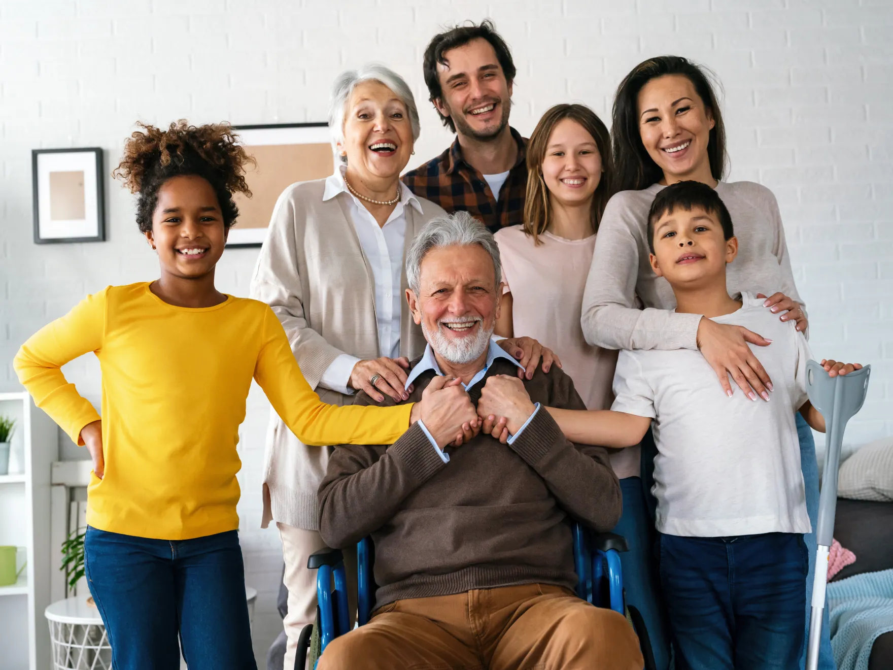 Smiling multigenerational family posing with an elderly man in a wheelchair in a cozy room.