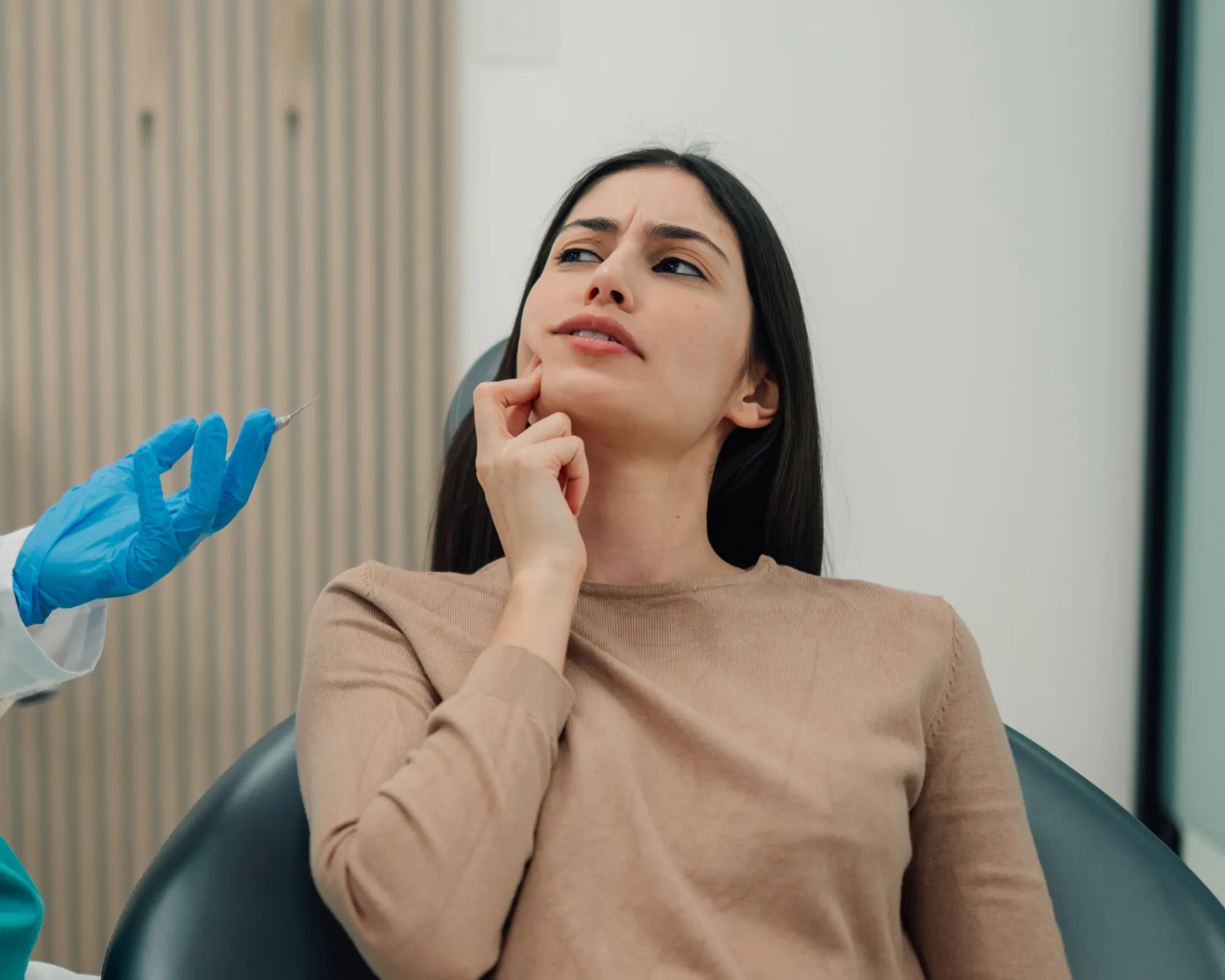 Woman touching her cheek with a concerned expression as a gloved hand holds a syringe nearby.