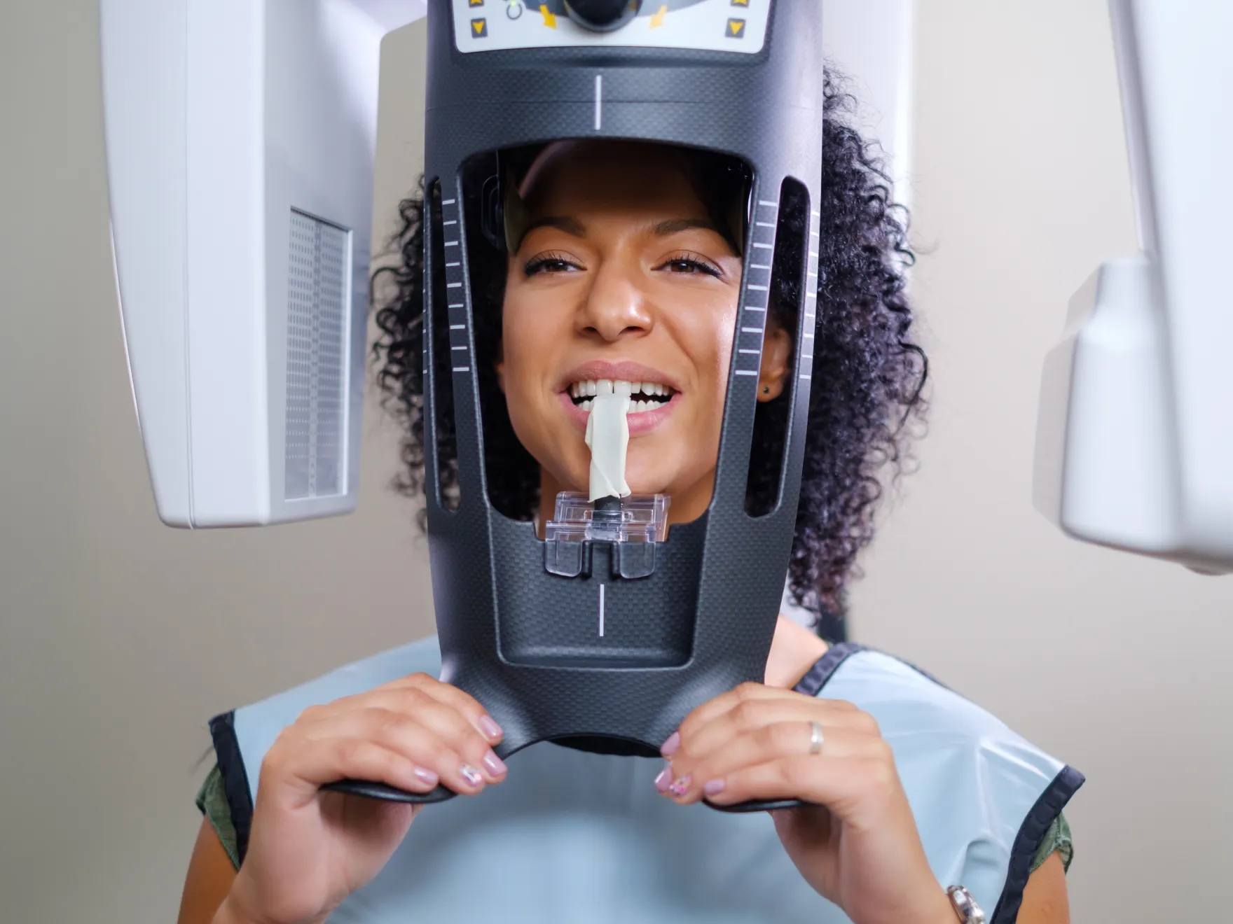 Woman undergoing dental X-ray with a bite block in her mouth and holding the X-ray device frame.