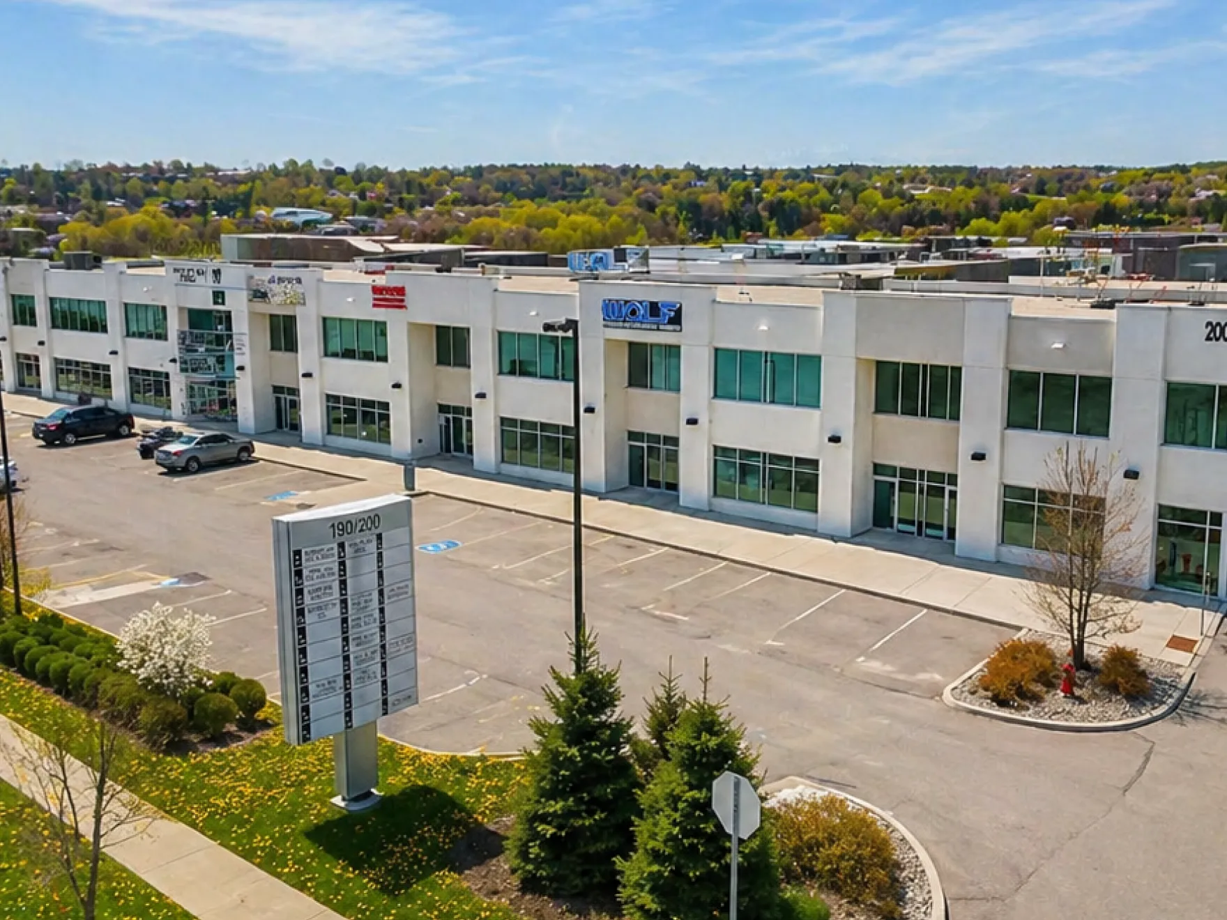 Exterior of white commercial building with parking lot, green trees, and businesses visible in windows.