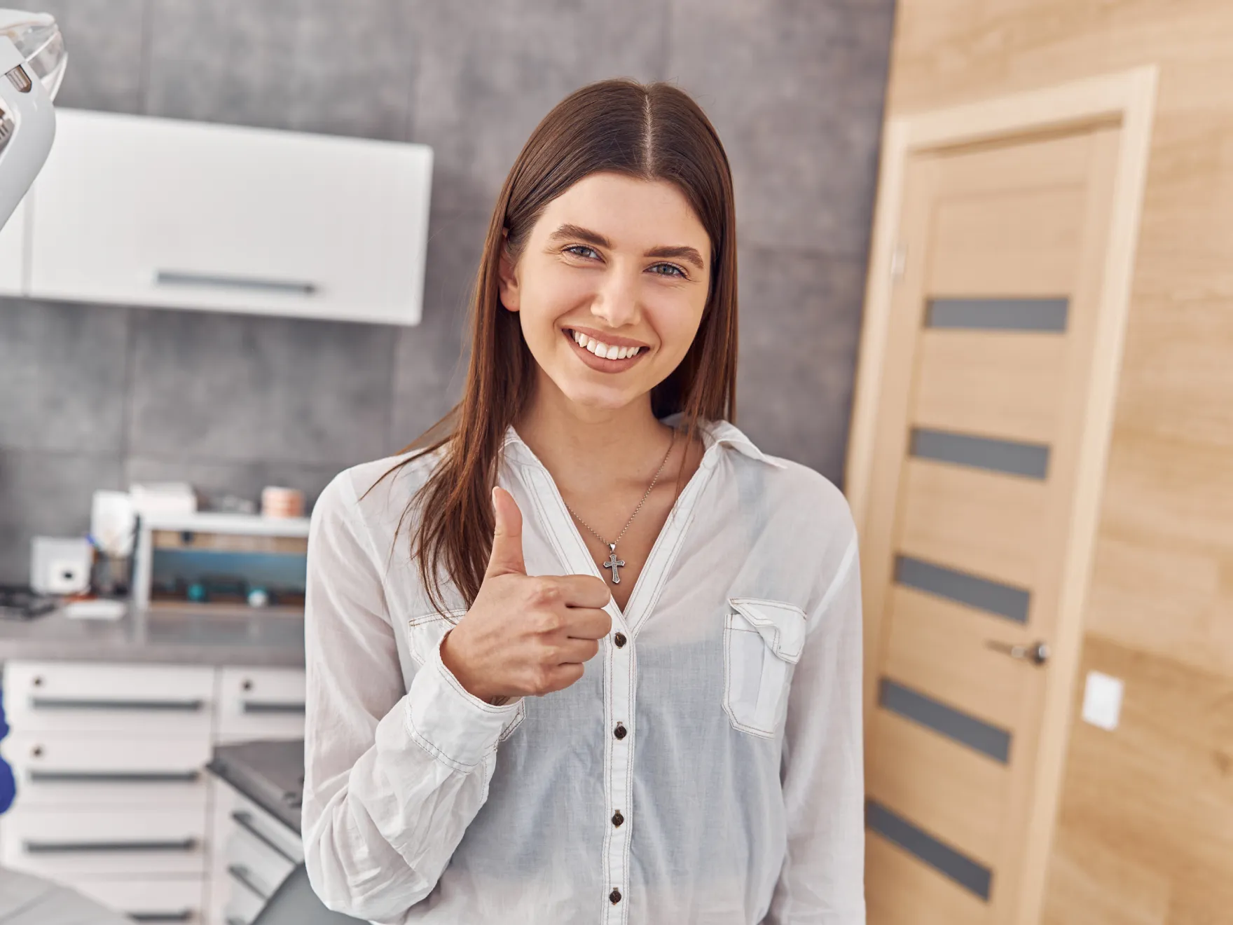 Smiling woman wearing a white blouse giving a thumbs-up in a modern kitchen.