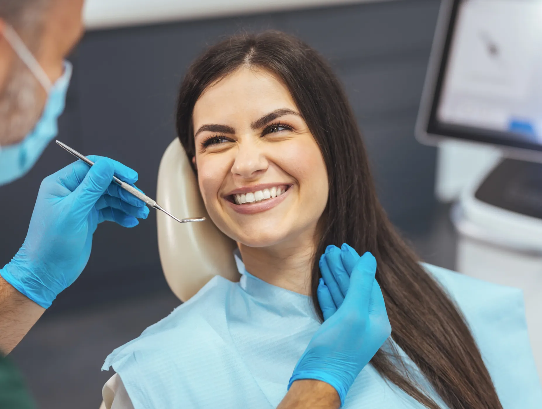 Smiling woman sitting in dental chair during checkup with dentist wearing blue gloves.